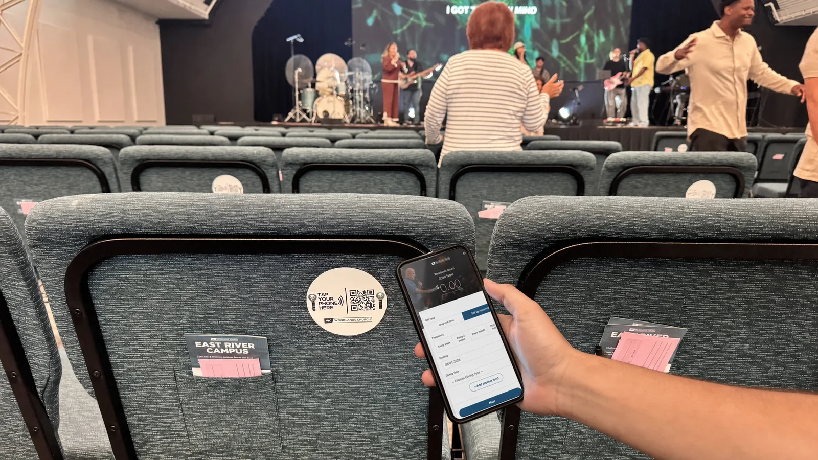 Rows of church chairs with tap-to-give plates on the seat backs, someone tapping a phone to one of them